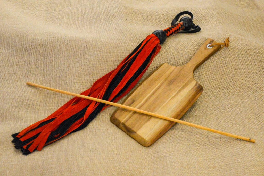 Photo by Liz BlackX
On the photo you see a black and red flogger, a bamboo cane and a paddle.
